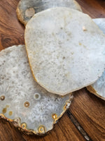 Natural agate stone slice coasters with textured crystalline patterns and gold-toned agate bodies, displayed on a rustic wooden surface.